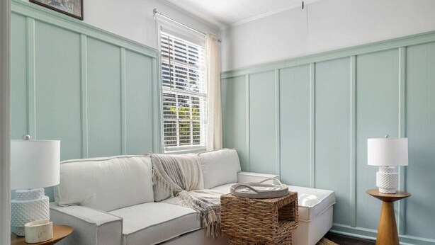 A room with a white sofa, a wicker side table, a small wooden side table, a wicker basket, and a window with blinds. - The Sweetgrass Suite - Newly Renovated - Downtown (Charleston)