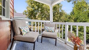 A covered porch with two cushioned chairs and a small table, surrounded by a white railing and a view of trees. - The Sweetgrass Suite - Newly Renovated - Downtown (Charleston)