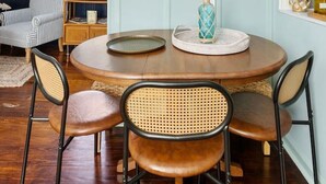 A dining area with a round table, four chairs, a large flat-screen TV mounted above, and a window with blinds. - The Sweetgrass Suite - Newly Renovated - Downtown (Charleston)