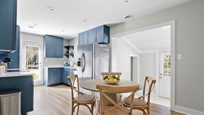 Une cuisine moderne avec des meubles bleus, un réfrigérateur en acier inoxydable et une table de salle à manger ronde en bois, accompagnée de quatre chaises.