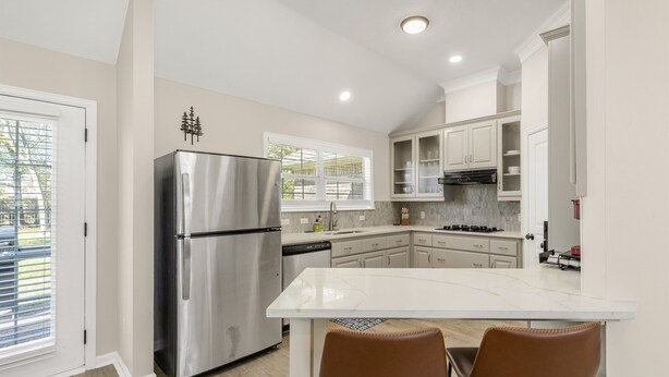A modern kitchen with a stainless steel refrigerator, white cabinets, and a central island with two chairs. - Augusta: 1 Mile from Texas A&M/Near Sorority Row (College Station)