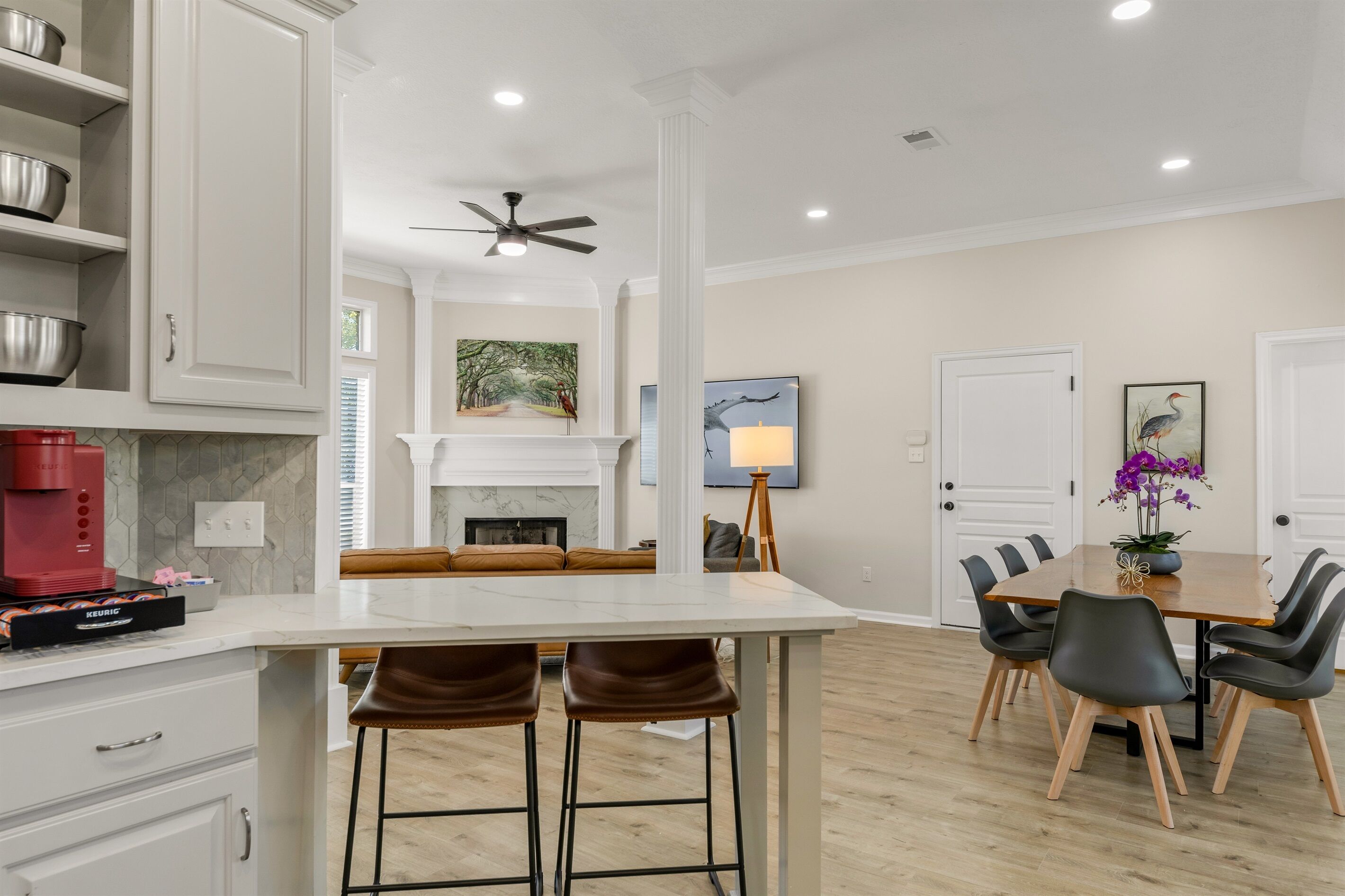 A modern kitchen with white cabinets, a coffee maker, and a dining area with a wooden table and chairs.