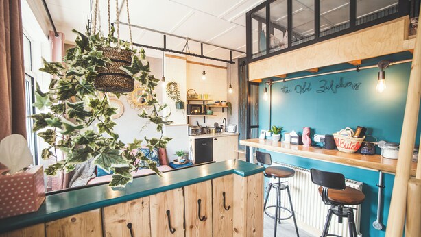 A cozy bar area with wooden bar stools, a teal countertop, and hanging plants. - Unique & stylish Loft Style Studio with Terrace, Parking & close to the beach (Stoke Fleming)