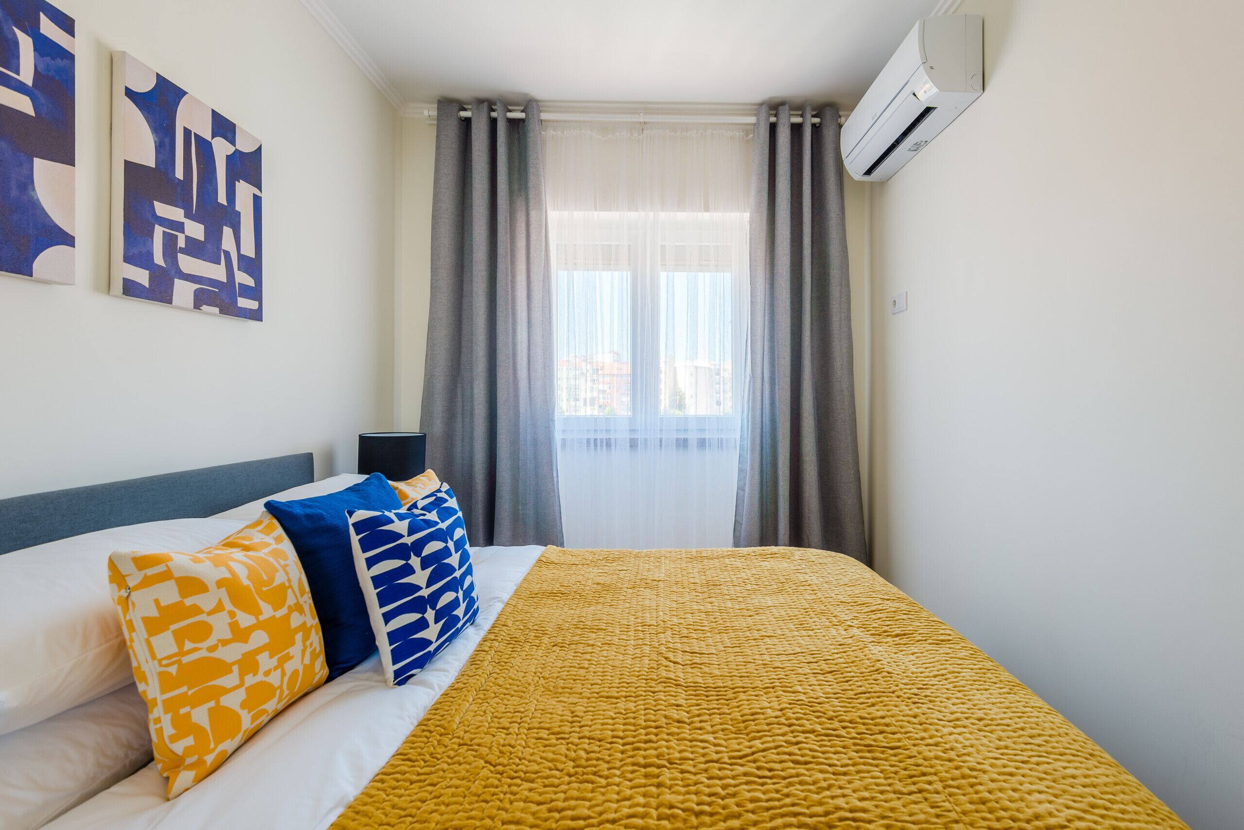 Une chambre d’hôtel avec un lit, une table de chevet, une fenêtre avec des rideaux et des œuvres d’art mural.