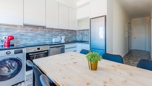 A compact kitchen with modern appliances, a wooden dining table, and a small potted plant. - Bela Vista C in Lisboa (Lisbon)