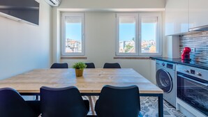 A modern kitchen with a washing machine, oven, and a dining area with a table and chairs. - Bela Vista C in Lisboa (Lisbon)