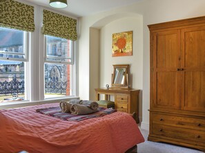 A bedroom with a bed, a wooden dresser, a window with a view of a building, and a painting on the wall.