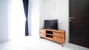 Ein Zimmer mit einem HolztV-Schrank, einer dunklen Tür und einem Fenster mit blauem Vorhang.