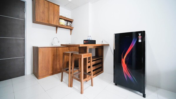 Une cuisine compacte avec des meubles en bois, un plan de travail, un évier et un réfrigérateur noir au design coloré.