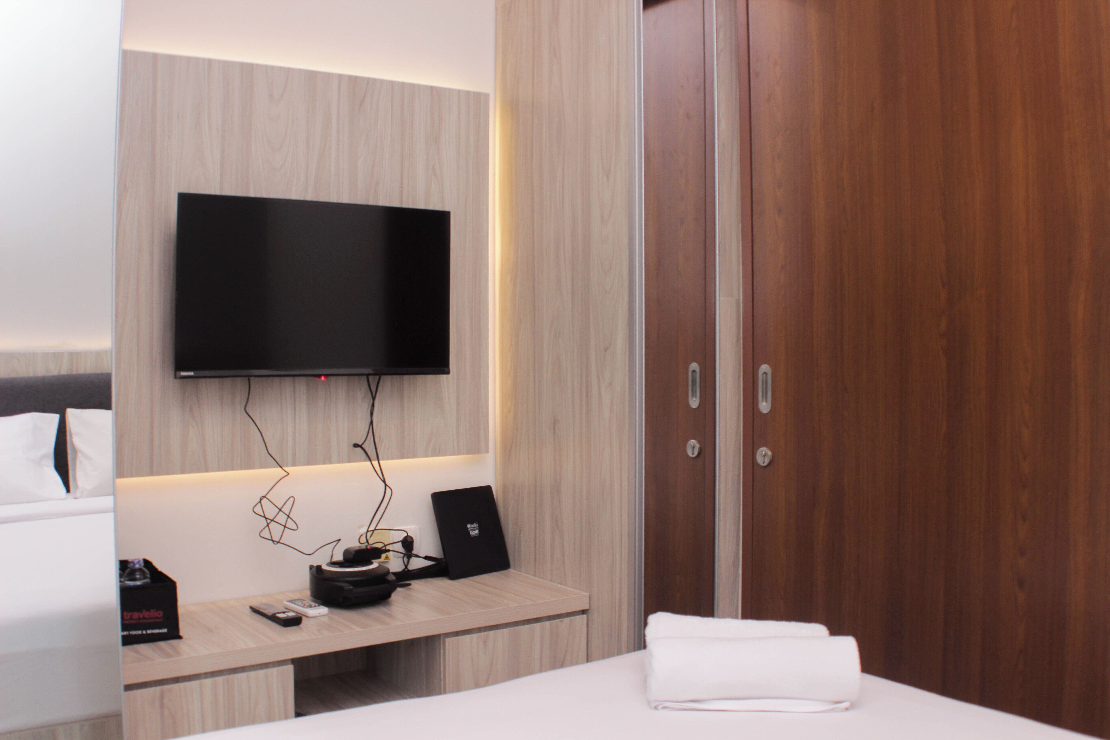 A hotel room with a bed, a desk with a laptop, a flat-screen TV mounted on the wall, and a wooden wardrobe.