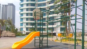 Un’area giochi con uno scivolo giallo e strutture per arrampicarsi, circondata da un edificio con diversi piani e finestre.