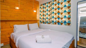 Une chambre d’hôtel avec une tête de lit en bois, une grande décoration murale aux motifs géométriques et un lit soigneusement fait, sur lequel est posée une serviette blanche.