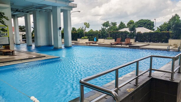 Une piscine dotée d’une rambarde en métal, de bancs et de chaises longues.