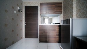 Uma cozinha compacta com armários de madeira escura, piso de azulejos brancos e uma geladeira.
