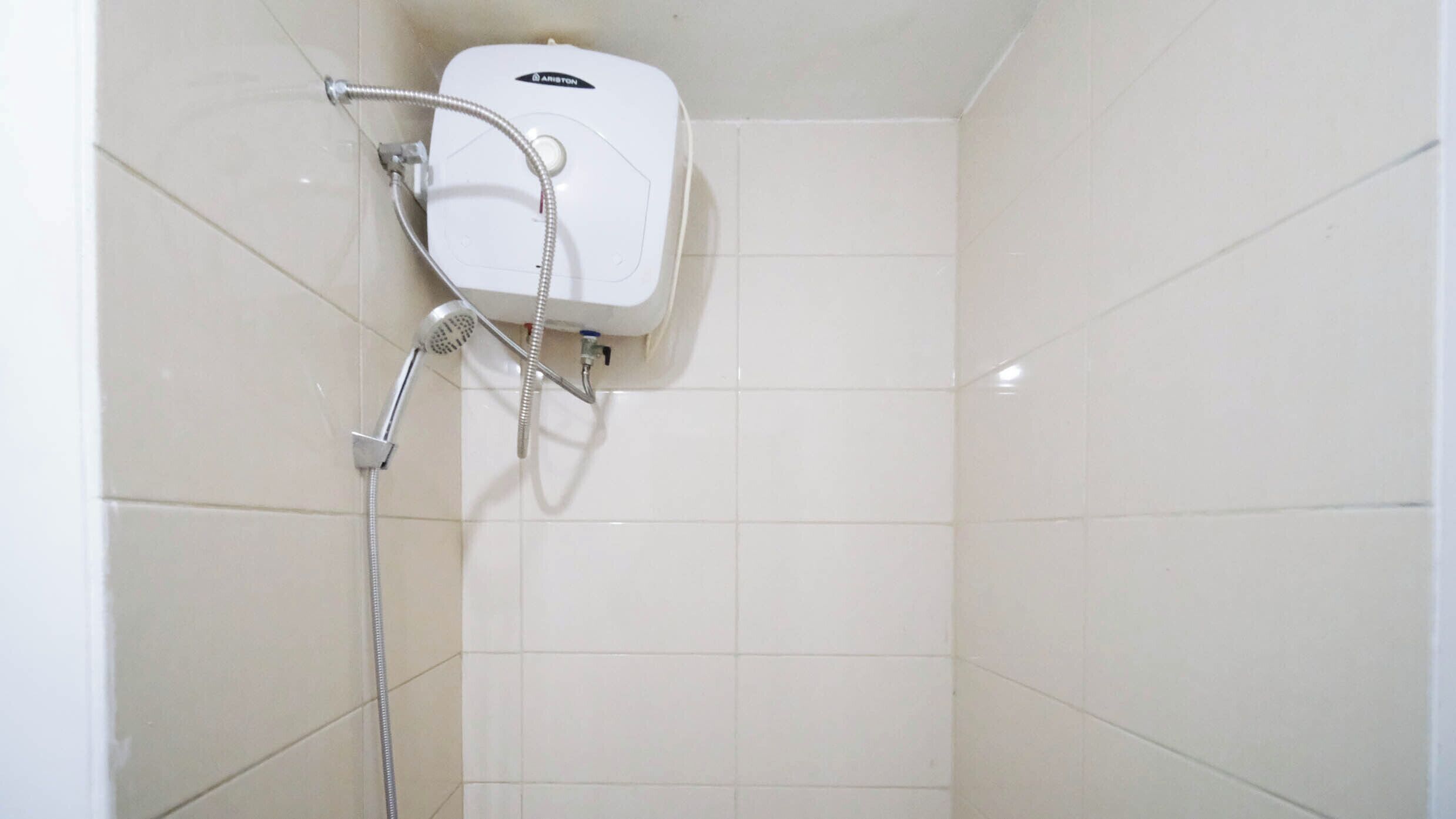 A bathroom with white tiled walls and a white shower unit with a handheld showerhead.