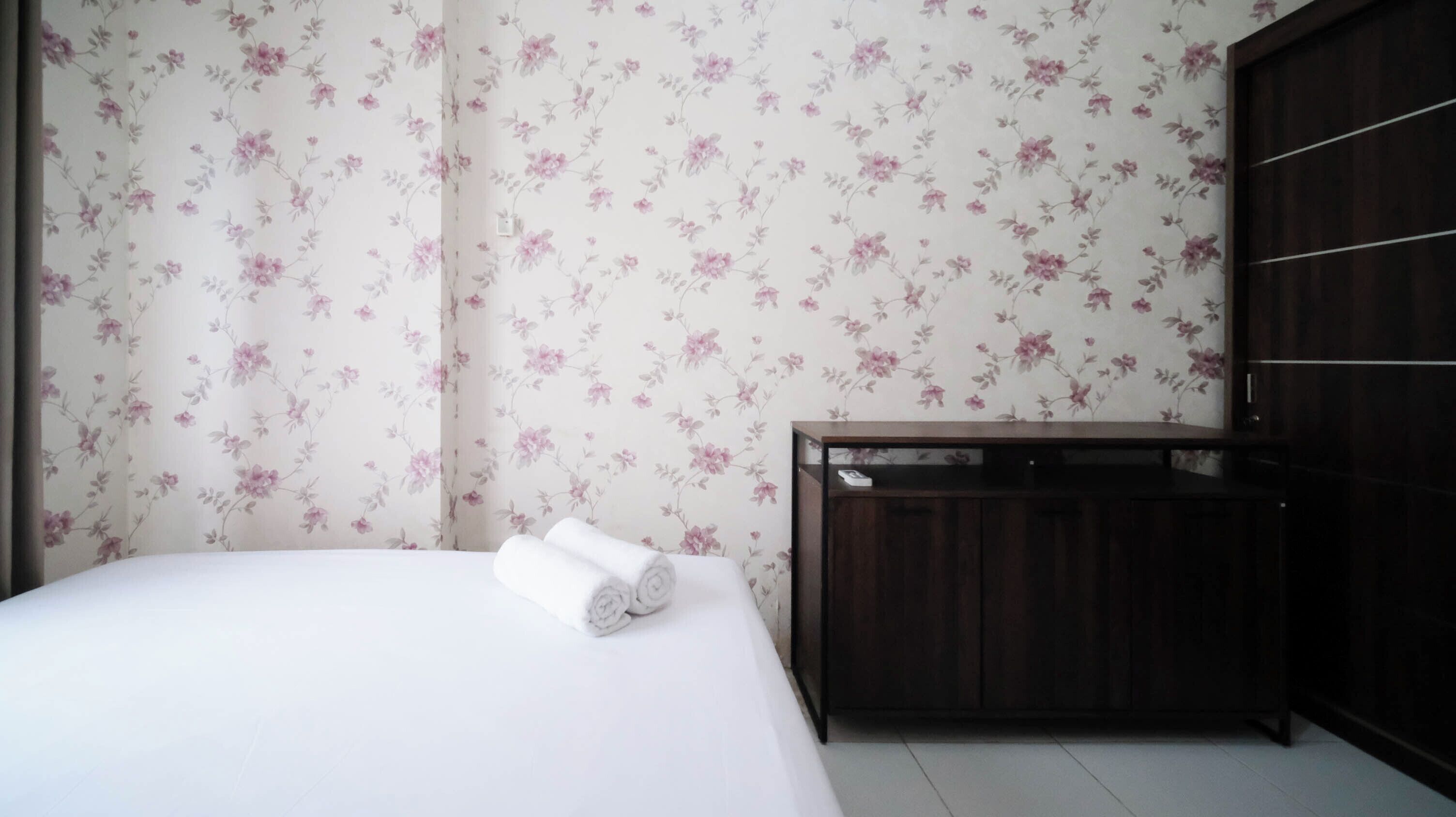 Una habitación de hotel con una cama, un armario de madera y papel tapiz con motivos florales.