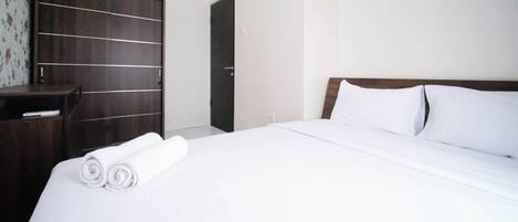 Una cama bien hecha con sábanas blancas y toallas enrolladas, un armario de madera y una pared lisa.