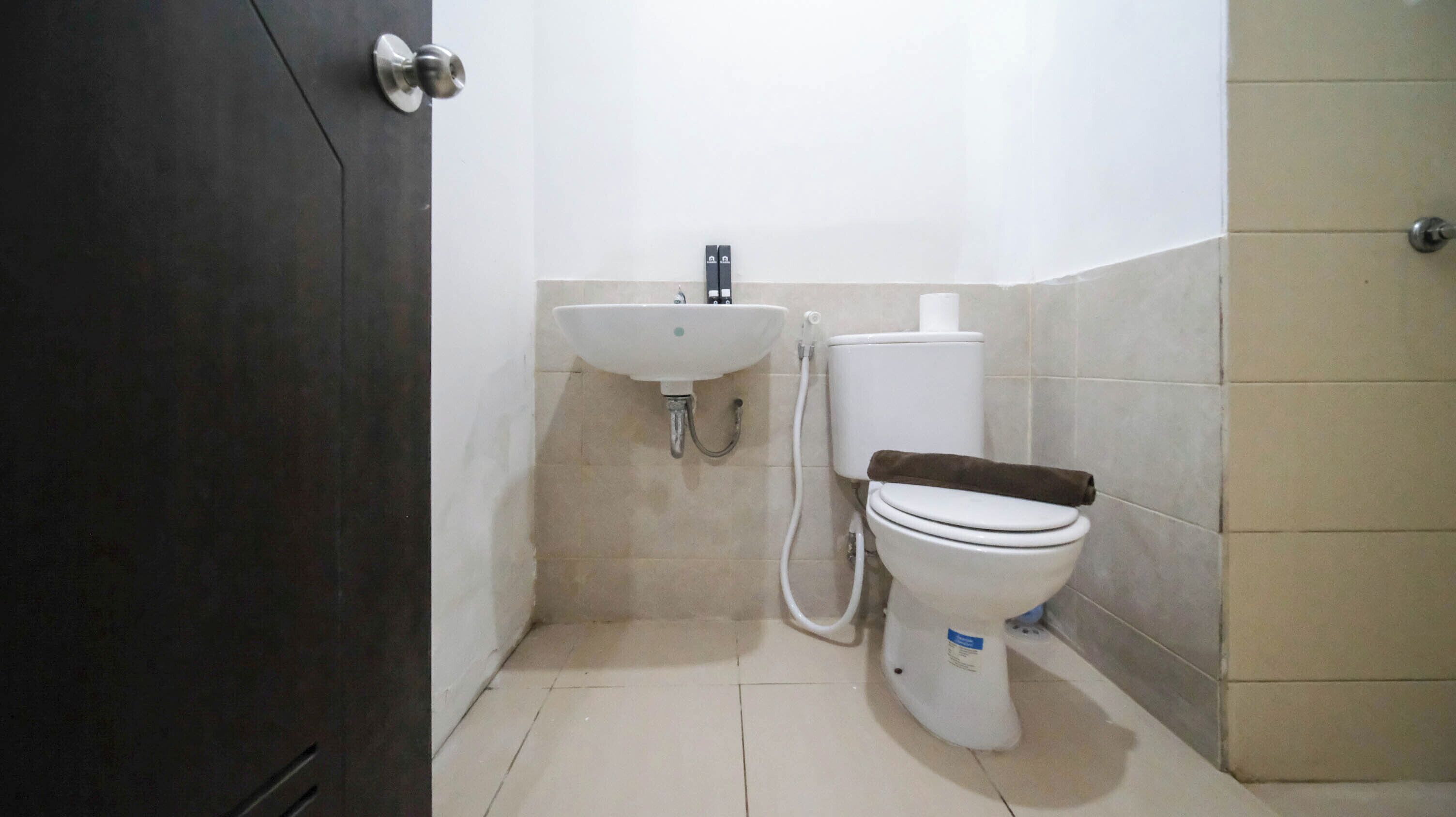 Ein kleines Badezimmer mit Toilette, Waschbecken und einer dunkel gefärbten Tür.