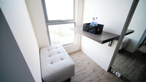 Ein kleiner, moderner Raum mit einer weißen gepolsterten Bank, Holzboden, einem Fenster und einem Regal mit zwei Wasserflaschen.