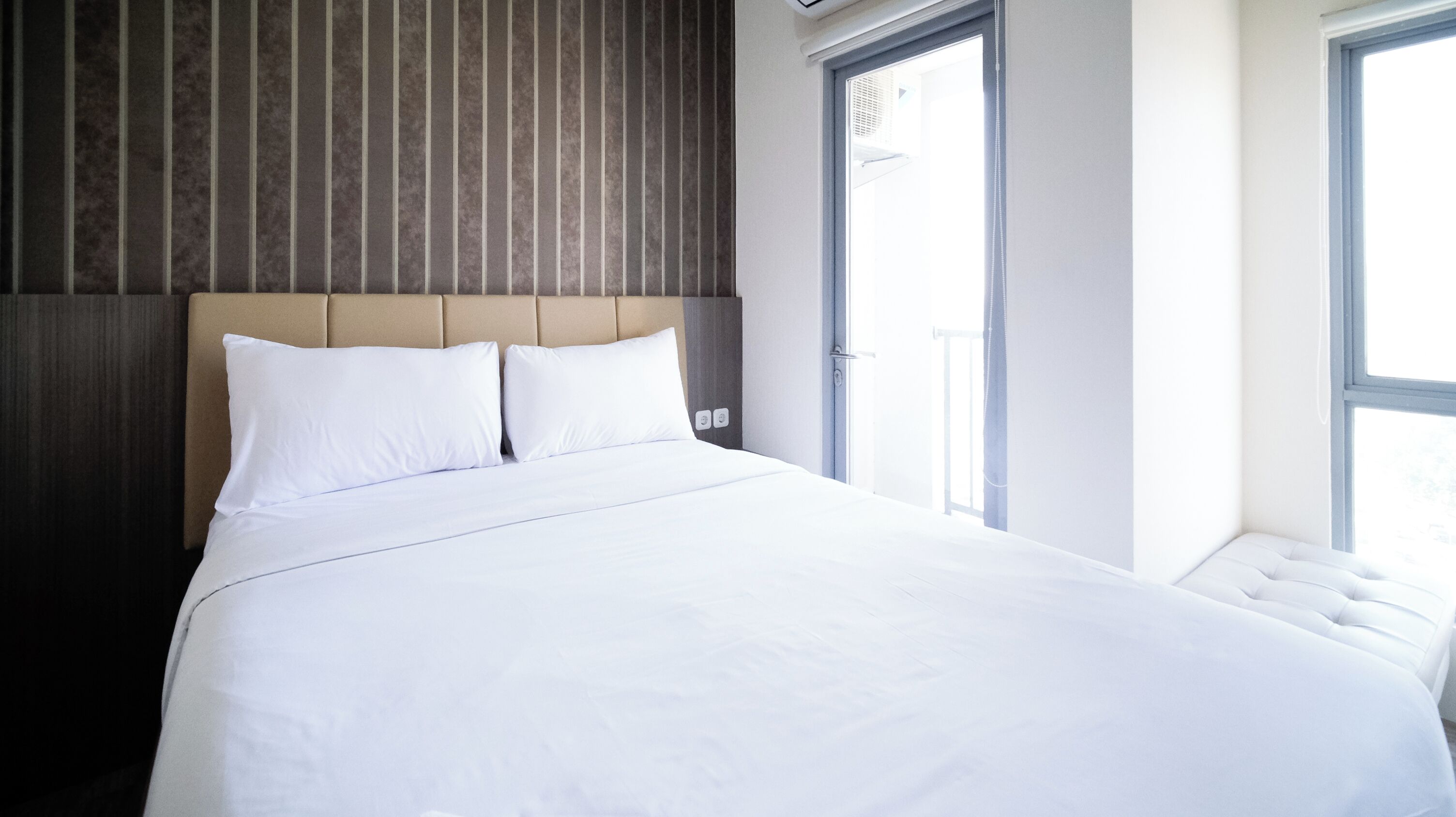 Une chambre d’hôtel moderne avec un grand lit, une tête de lit en bois et deux fenêtres.