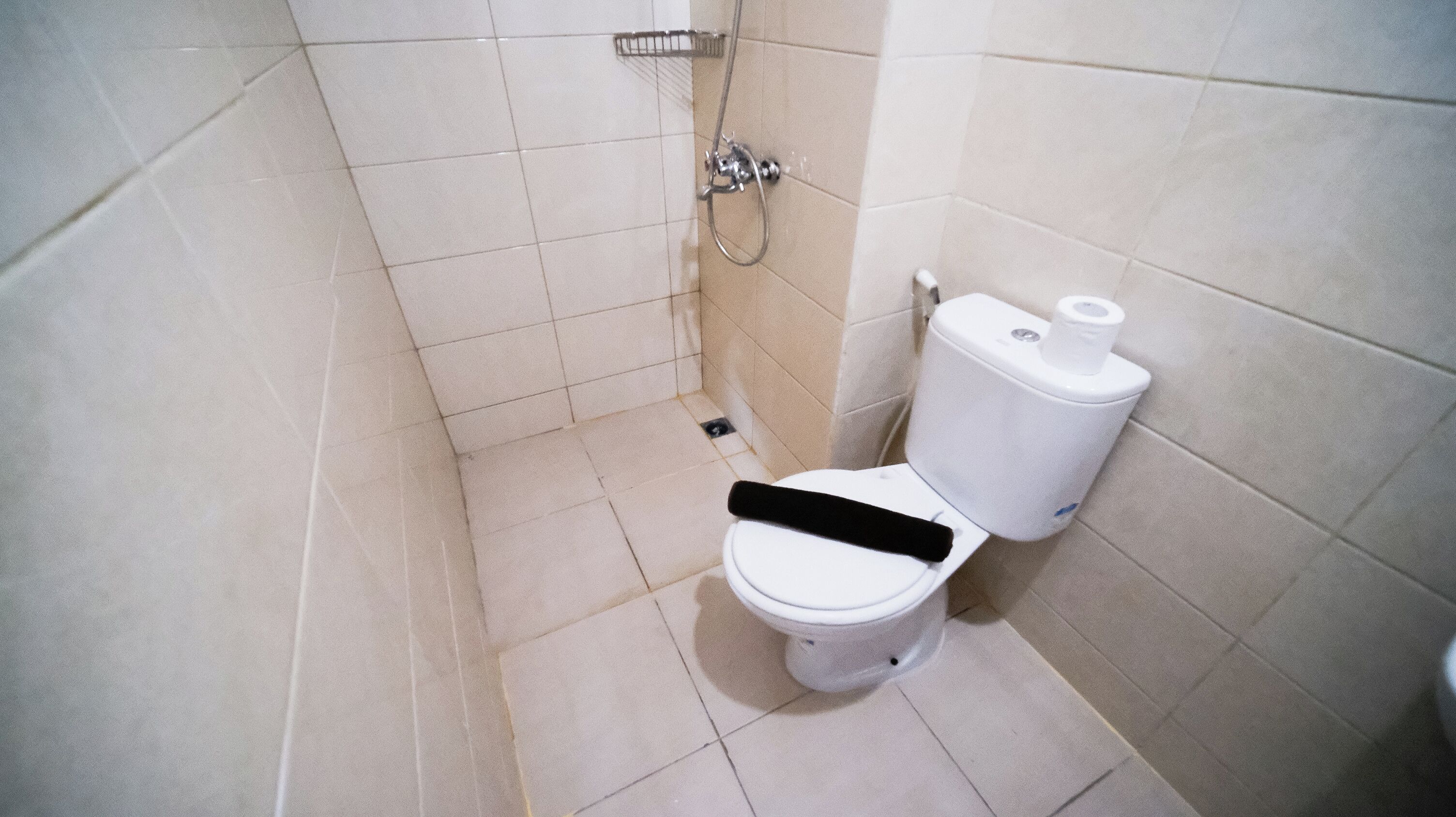 A small, tiled bathroom with a toilet, a shower, and a toilet paper holder.