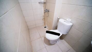 A small, tiled bathroom with a toilet, a shower, and a toilet paper holder.