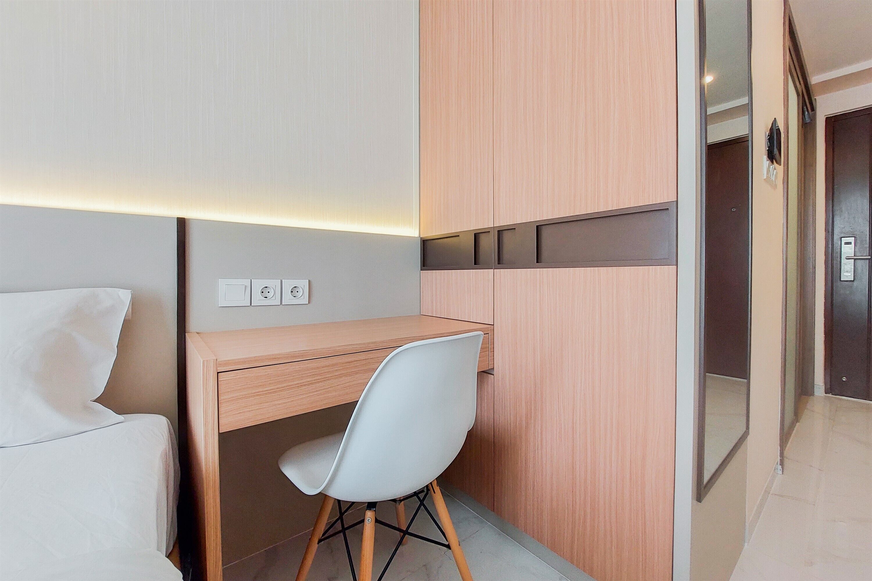 Una habitación de hotel moderna con un escritorio de madera, una silla blanca y una cama con ropa de cama blanca.