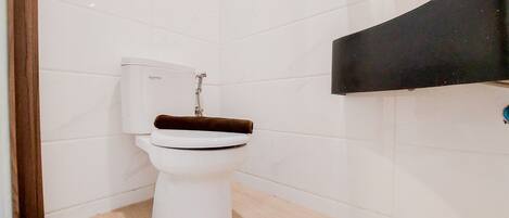 Une salle de bain avec des toilettes blanches, une serviette noire et un mur recouvert de carreaux blancs.