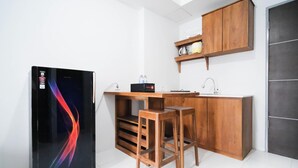 A compact kitchen with a refrigerator, wooden stools, a countertop, and a shelf above the sink. - Tidy And Cozy 1Br At Tamansari Prospero Sidoarjo Apartment (Sidoarjo)