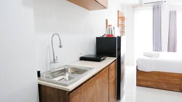 Una kitchenette compacta con un lavamanos de acero inoxidable, una estufa portátil negra y un mueble de madera.