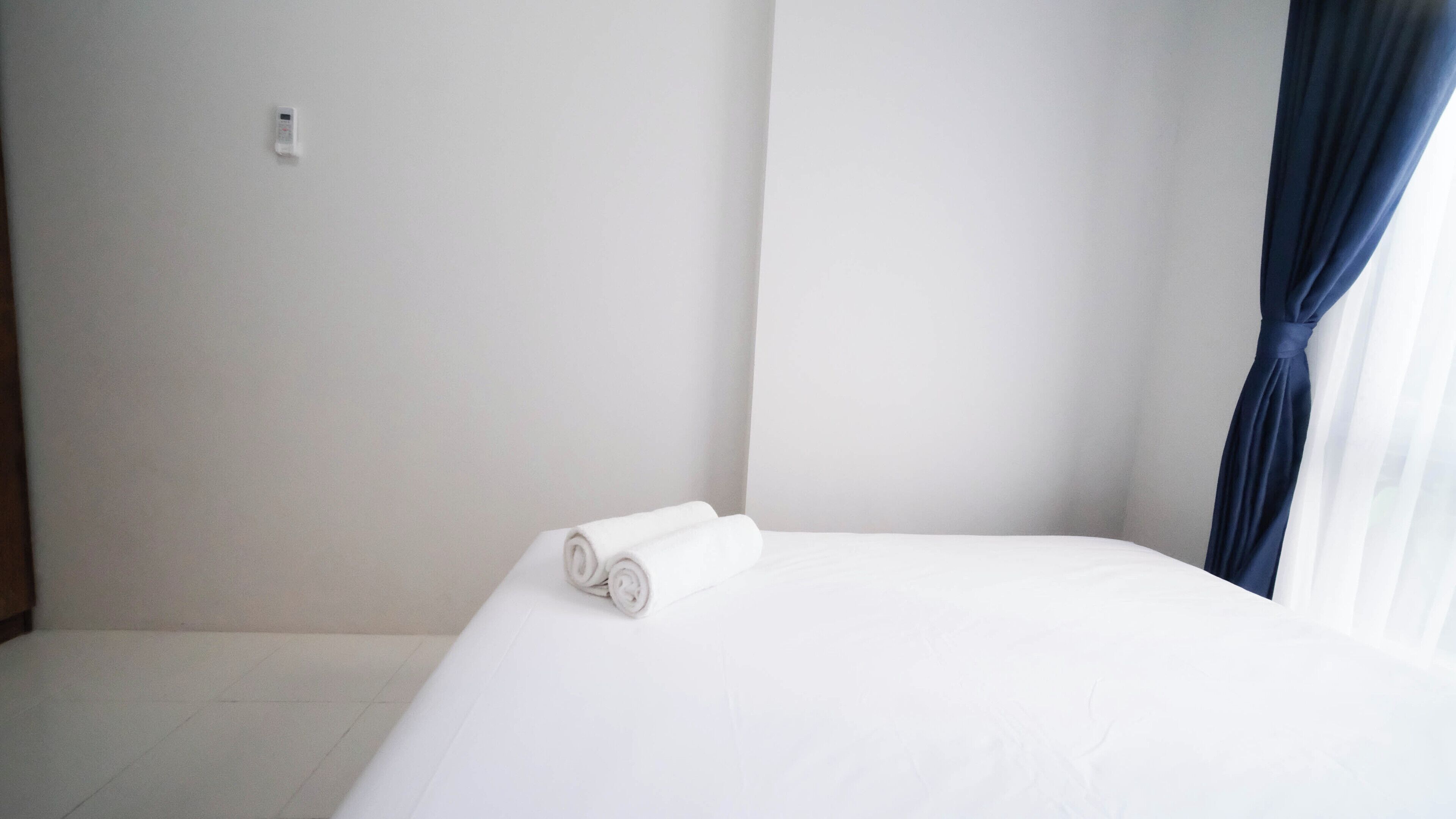 Habitación de hotel con una cama bien hecha, un enchufe en la pared y una ventana con cortina oscura.