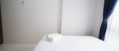 Habitación de hotel con una cama bien hecha, un enchufe en la pared y una ventana con cortina oscura.