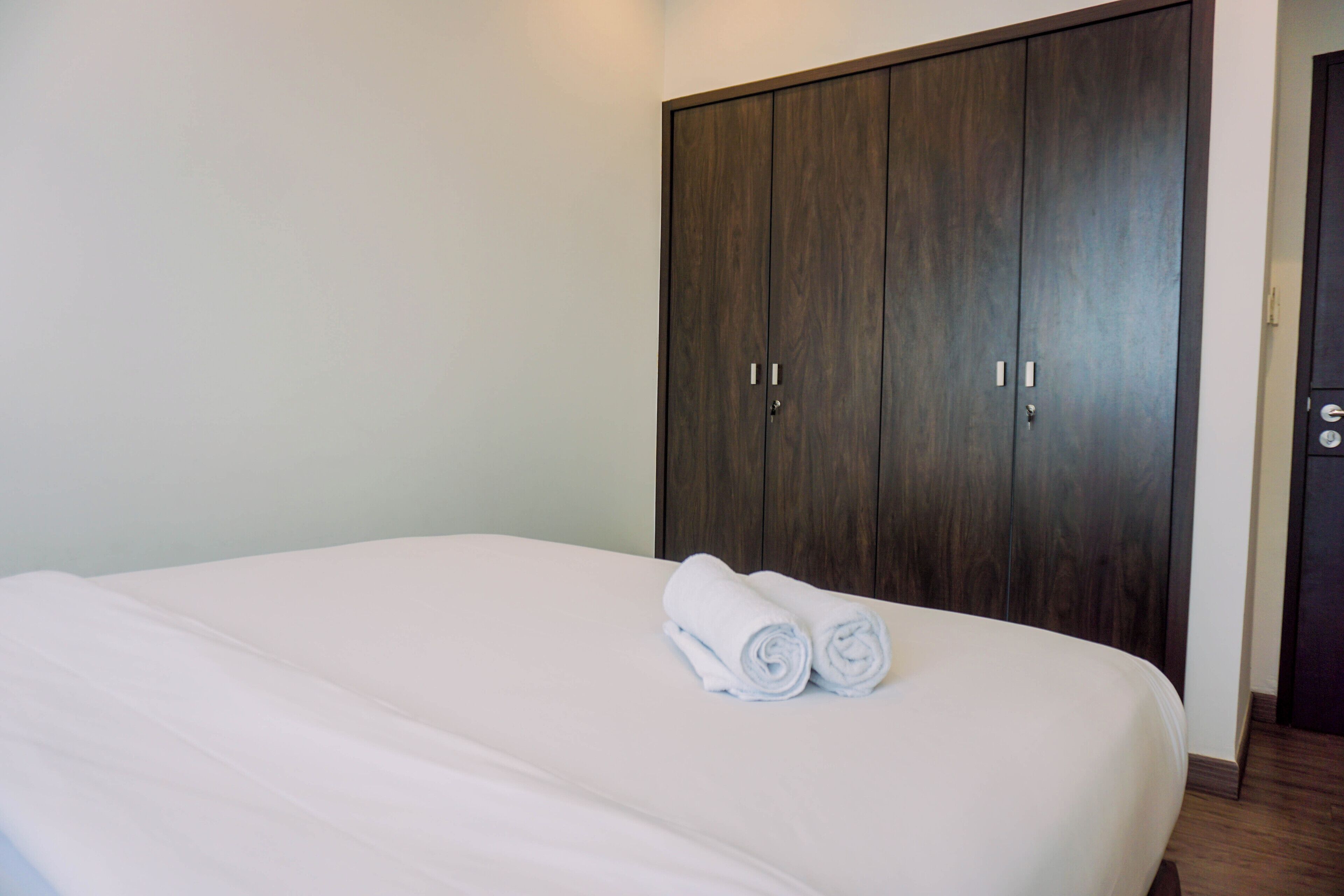 Habitación de hotel con una cama grande, un armario de madera oscura y dos toallas enrolladas sobre la cama.