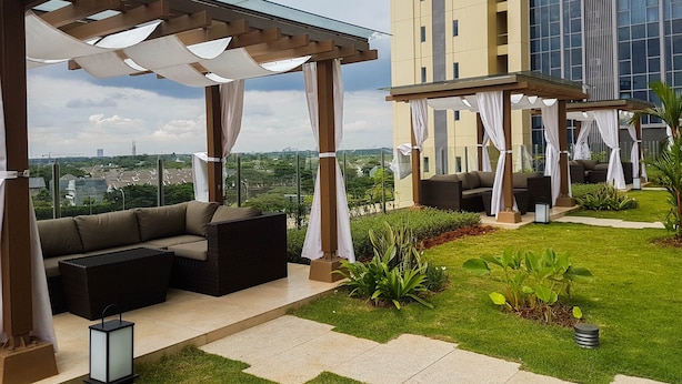 A rooftop patio with outdoor seating, a glass balustrade, and a view of a cityscape. - Nice 2Br At Branz Bsd City Apartment (Pagedangan)