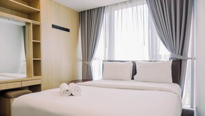 A hotel room with a large bed, a wooden wardrobe, a mirror, and a window with curtains. - Nice 2Br At Branz Bsd City Apartment (Pagedangan)