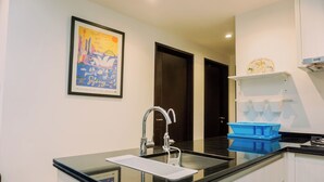 A modern kitchen with a black countertop, stainless steel sink, and a framed cityscape artwork on the wall. - Nice 2Br At Branz Bsd City Apartment (Pagedangan)