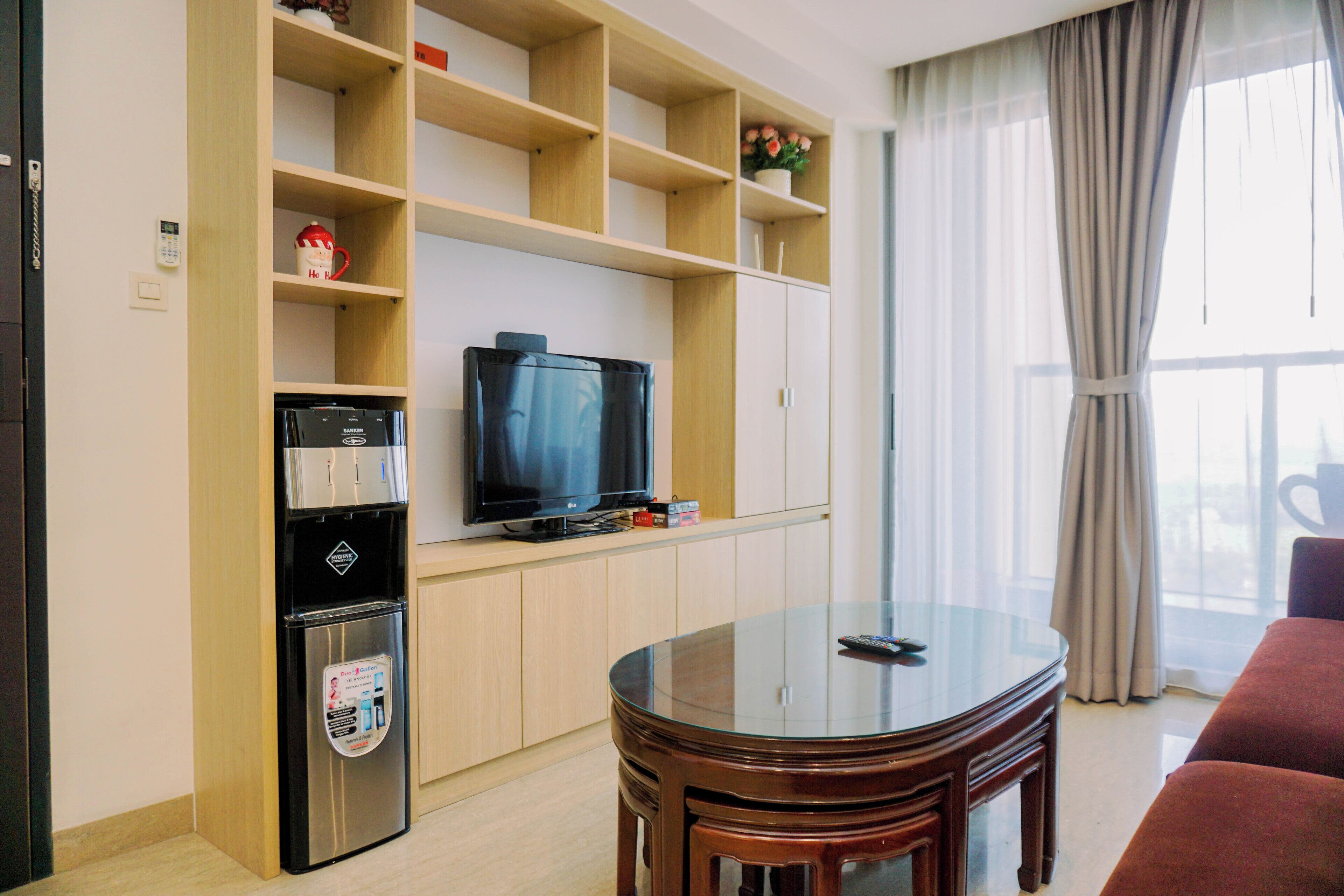 Una sala de estar con un televisor de pantalla plana, estanterías de madera, una cafetera y una mesa de vidrio.