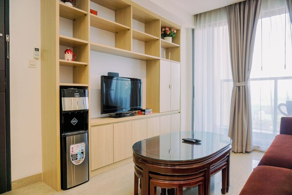 Una sala de estar con un televisor de pantalla plana, estanterías de madera, una cafetera y una mesa de vidrio.