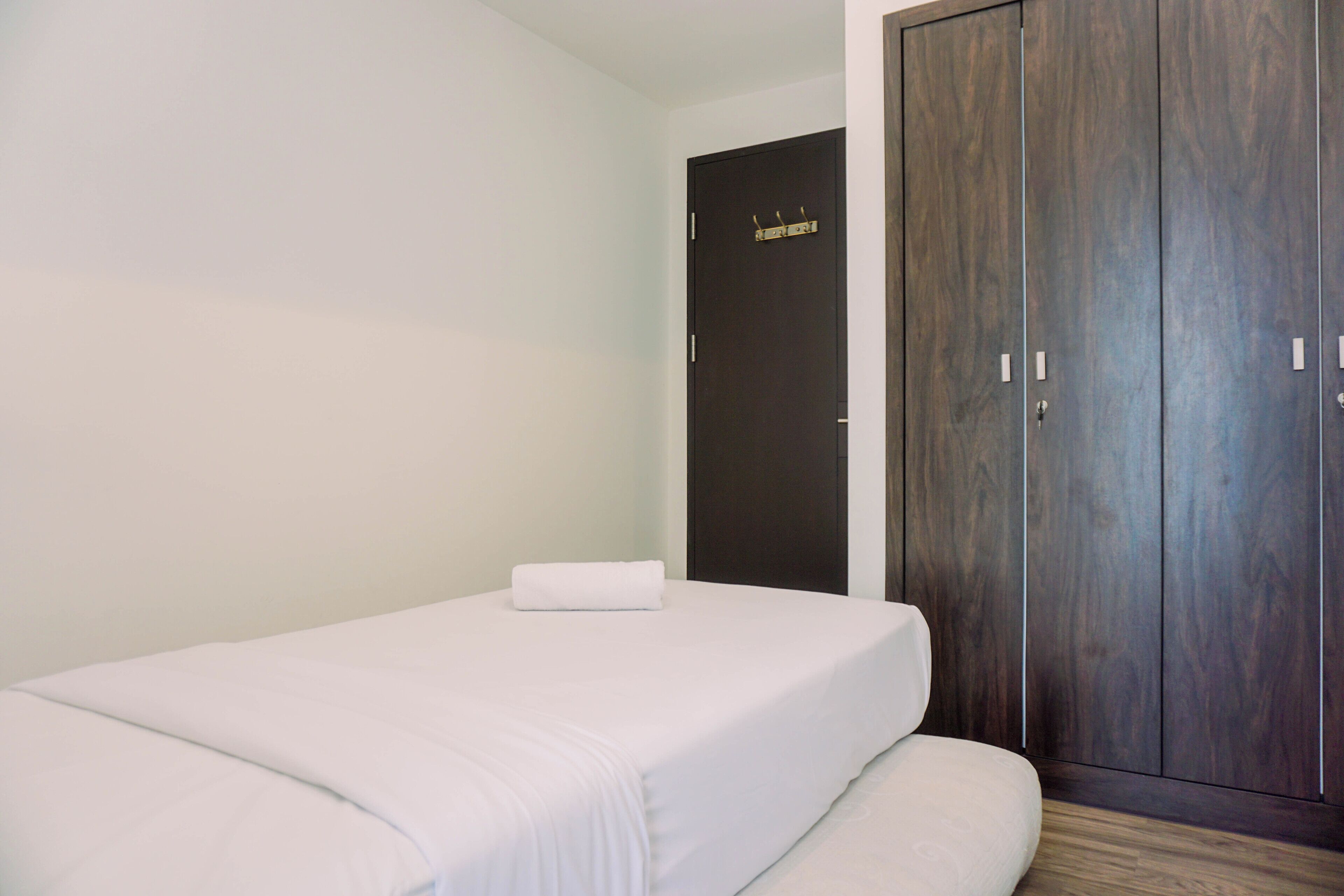 A single bed with white bedding, a dark wooden wardrobe, and a plain wall.