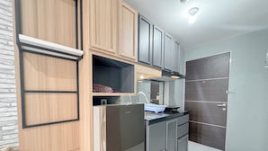 A compact kitchen with wooden cabinets, a stainless steel refrigerator, and a tiled backsplash. - Comfortable Living Studio At Tamansari Prospero Apartment (Sidoarjo)