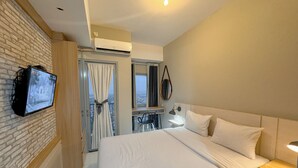 Ein Hotelzimmer mit Bett, Wandfernseher, Klimaanlage, Fenster mit Vorhängen, Nachttisch mit Lampe und Spiegel.
