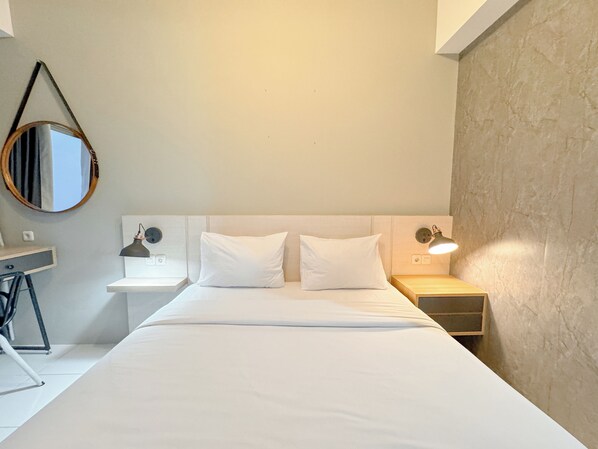 A neatly arranged hotel room with a bed, bedside tables, a lamp, and a mirror. - Cozy Stay And Best Value Studio At Tamansari Prospero Apartment (Sidoarjo)