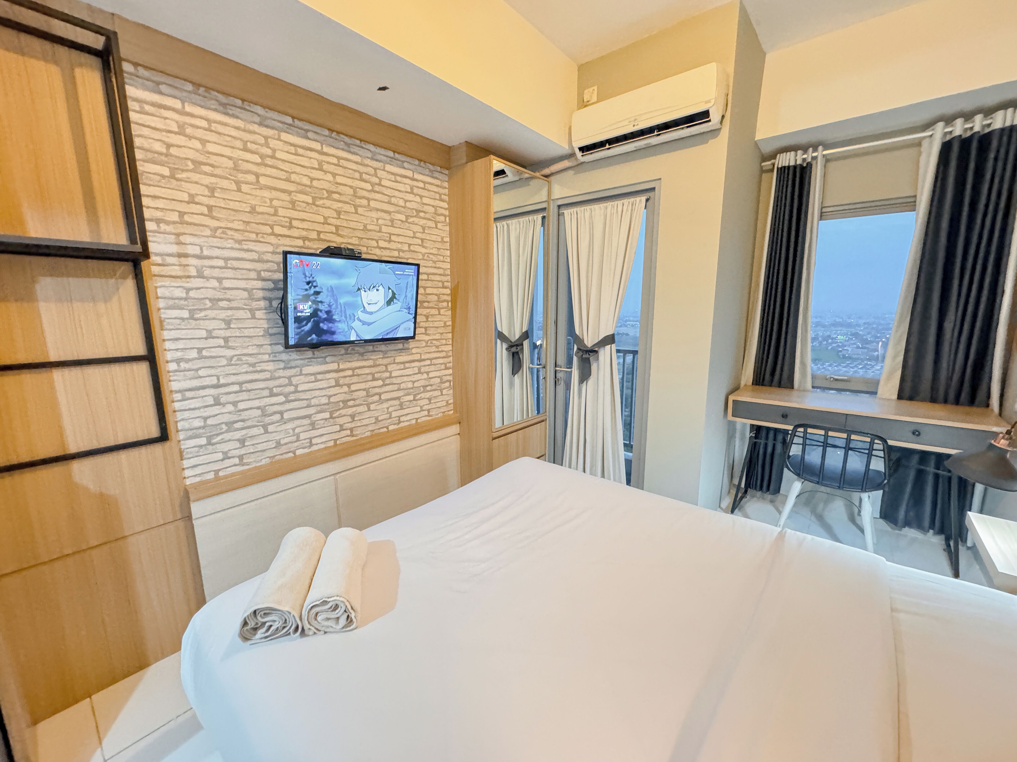 Habitación de hotel con una cama, un televisor instalado en una pared de ladrillo, una ventana con cortinas y un equipo de aire acondicionado.