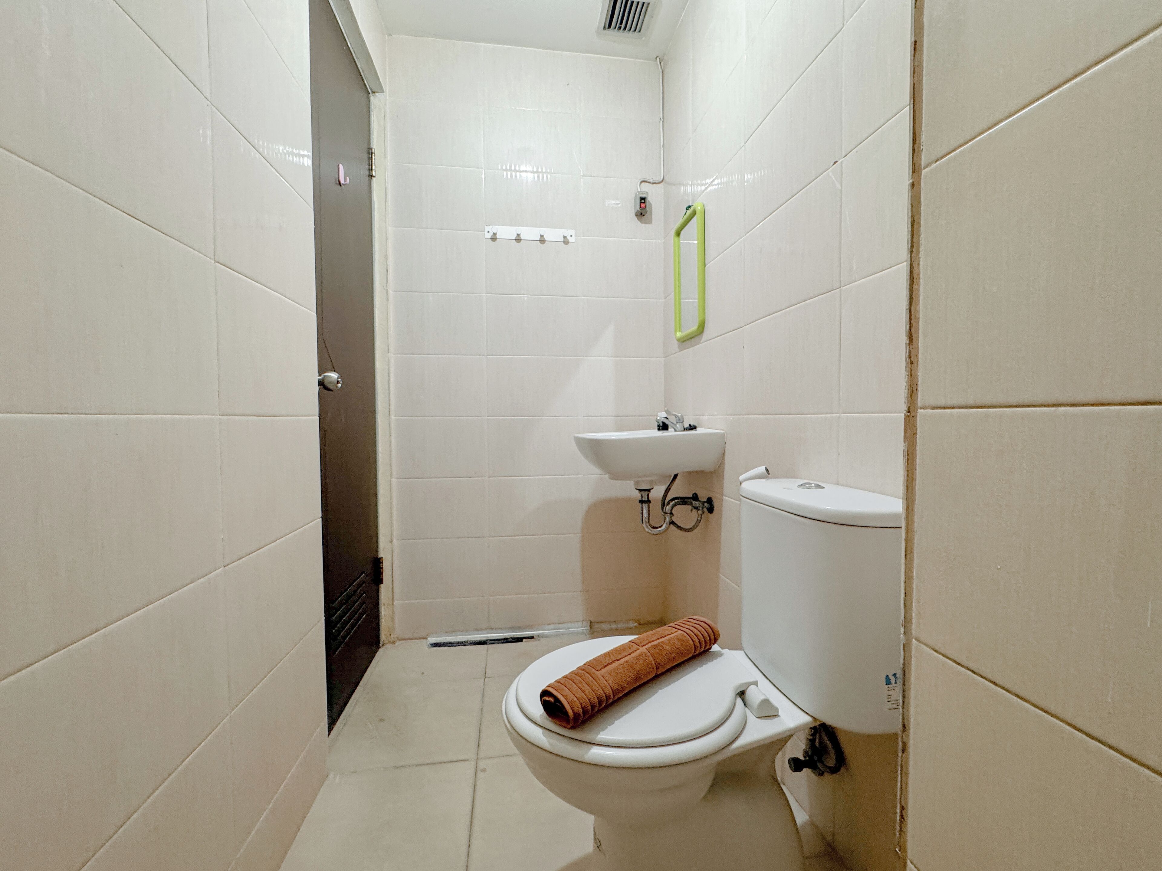 Un baño pequeño y limpio con azulejos blancos, inodoro, lavamanos y zona de ducha.