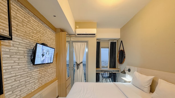 Ein Hotelzimmer mit Fernseher an der Wand, einem Bett mit weißer Bettwäsche, einem Schreibtisch mit Stuhl und Blick auf die Stadt durch das Fenster.
