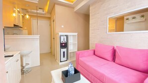 Una sala moderna con un sofá rosa, una mesa de centro blanca con una botella de agua, un armario blanco y un dispensador de agua.