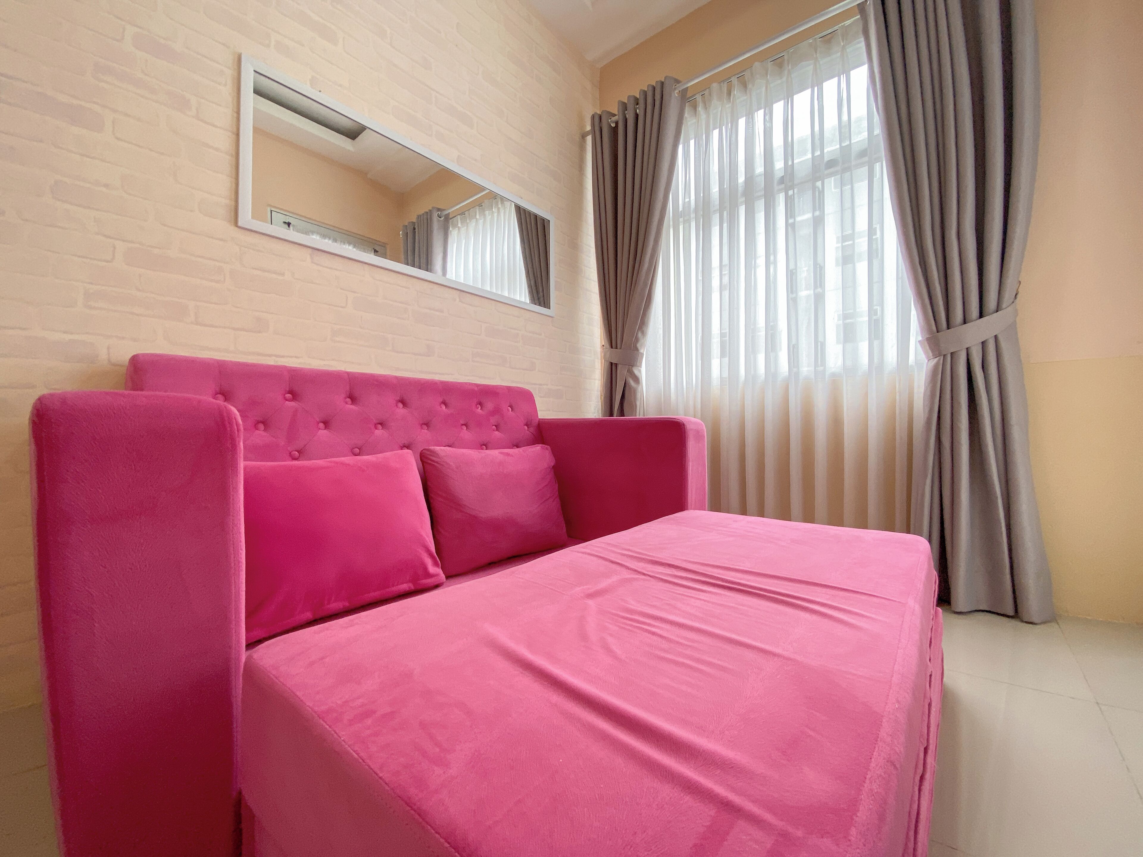 Una habitación con una cama rosa, un espejo en la pared y una ventana con cortinas.