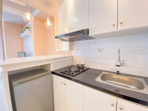 A modern kitchen with white cabinets, a black countertop, a gas stove, and a stainless steel sink. - The Nifty Nook 2Br At Grand Asia Afrika Apartment (Bandung)