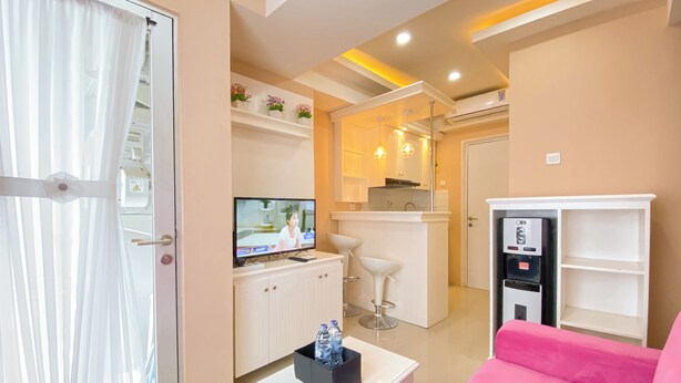 Una habitación de hotel moderna con televisión, minibar, sofá rosa y una pequeña cocina.