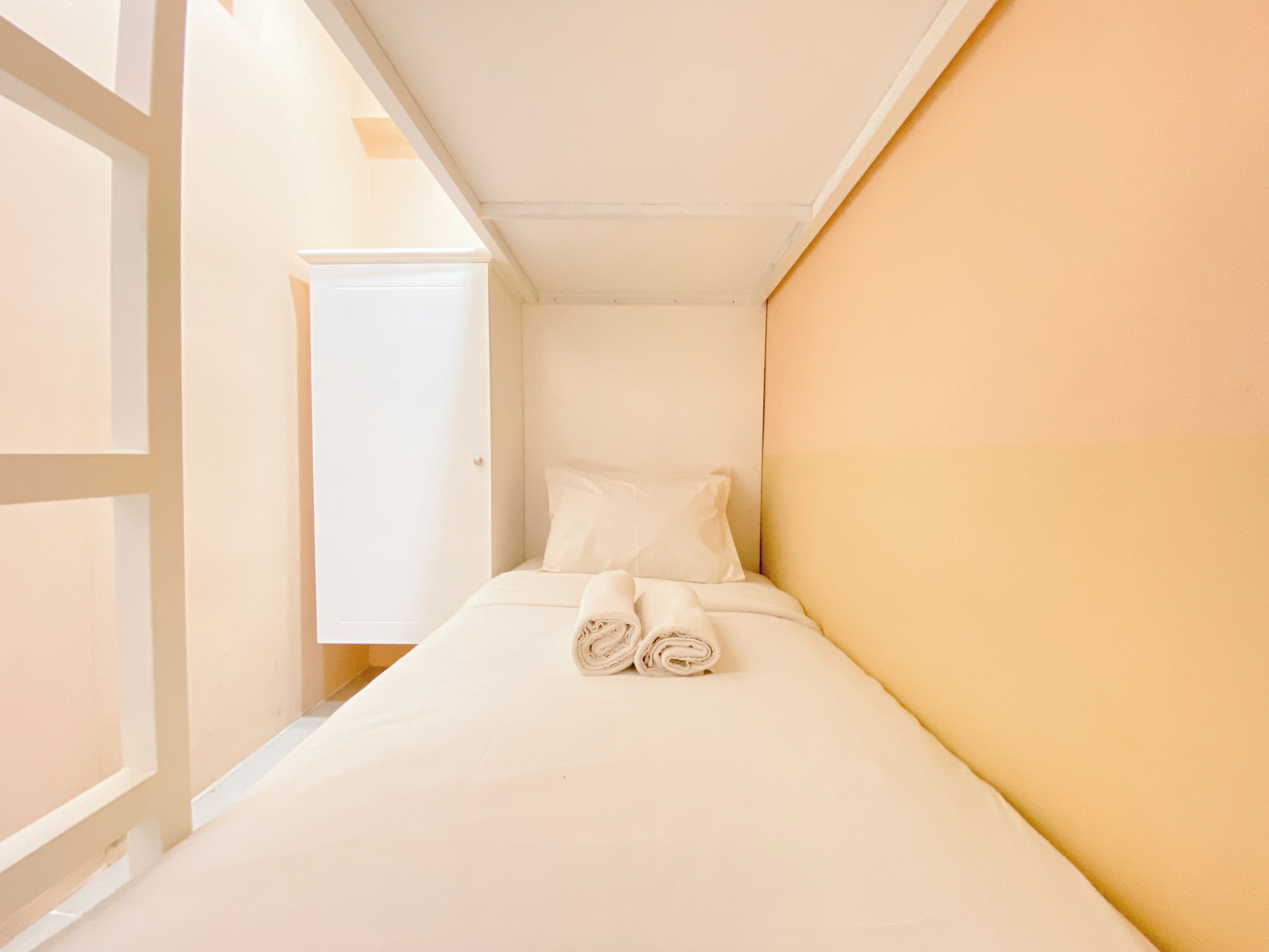 A small, single-bed room with a plain white bed and a white headboard.